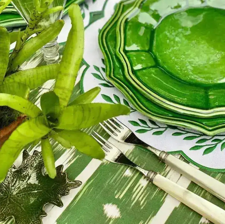 leafy lace placemat close-up with green leaf embroidery border under stacked green ceramic plates on ikat-stripe cloth