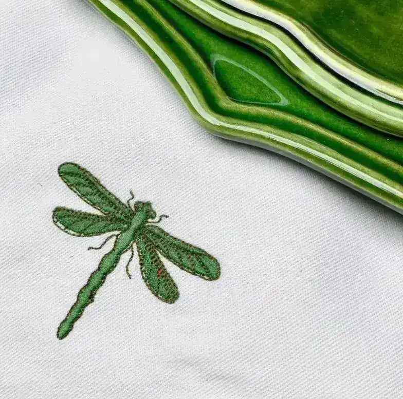 leafy lace placemat macro detail of green dragonfly embroidery on white linen with green ceramic plate at edge