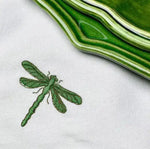 leafy lace placemat macro detail of green dragonfly embroidery on white linen with green ceramic plate at edge