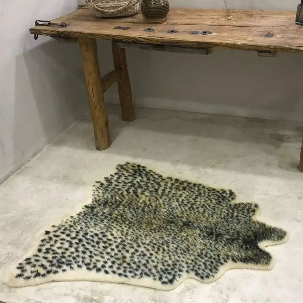 A stylish leopard print faux cowhide area rug placed on a smooth concrete floor, enhancing an elegant rustic wooden table setting. Perfect for large living rooms, this 8x10 living room rug offers a bold and chic statement piece.