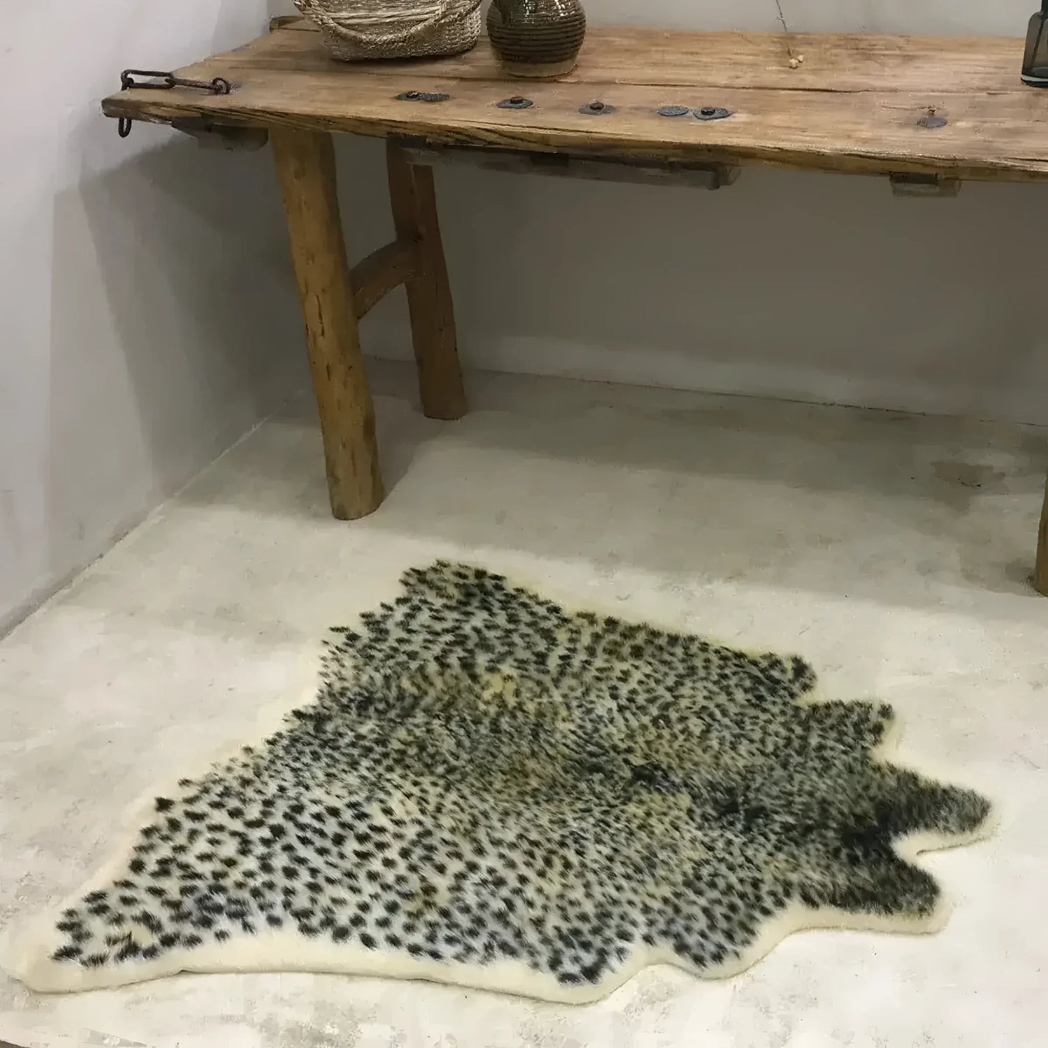 A stylish leopard print faux cowhide area rug placed on a smooth concrete floor, enhancing an elegant rustic wooden table setting. Perfect for large living rooms, this 8x10 living room rug offers a bold and chic statement piece.