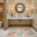 Bathroom with decorative wallpaper, round mirror, and floral rug.