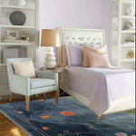 A contemporary area rug with a soothing blue and orange abstract design placed in a modern bedroom with a white bed, pastel pillows, and elegant decor. This wool rug adds a touch of sophistication and warmth to the living room area.