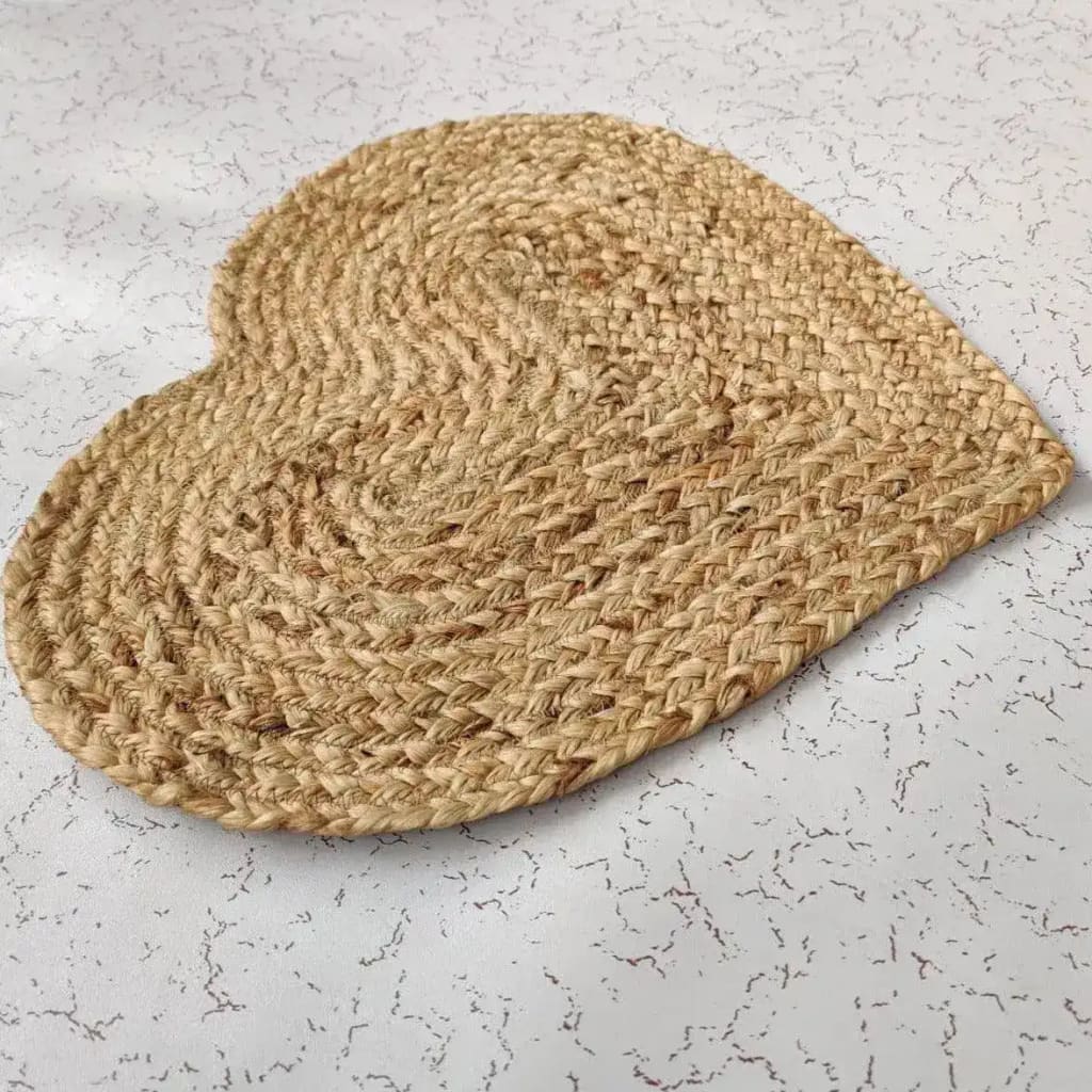 A beautifully crafted heart-shaped jute rug placed on a light-colored, patterned floor. This round area rug is ideal for adding a natural touch to any dining room, serving as an elegant dining room carpet or a large area rug centerpiece.