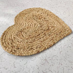 A beautifully crafted heart-shaped jute rug placed on a light-colored, patterned floor. This round area rug is ideal for adding a natural touch to any dining room, serving as an elegant dining room carpet or a large area rug centerpiece.