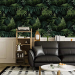 Lush green fern jungle wallpaper above white panelling with black leather sofa and shelf