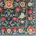 A beautifully detailed area rug showcasing a lush floral design, perfect for adding a vintage touch to any dining room or living room. This hand-tufted wool rug features vibrant red, yellow, and cream flowers against a rich blue background, ideal for creating a warm and inviting space.