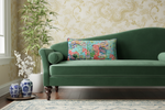Green sofa with a colorful pillow in a room with decorative wallpaper and plants.