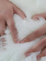 Close-up of a luxurious plush soft sheepskin area rug, showcasing its fluffy texture as hands gently press into the white fibers. Ideal for large living room rugs, especially in sizes like 8x10.