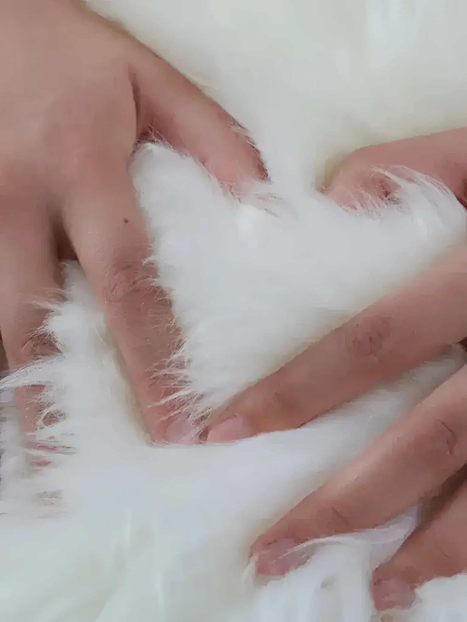 Close-up of a luxurious plush soft sheepskin area rug, showcasing its fluffy texture as hands gently press into the white fibers. Ideal for large living room rugs, especially in sizes like 8x10.