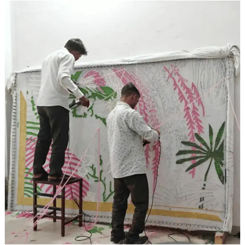 Artisans meticulously crafting a made-to-order hand-tufted wool rug, perfect for dining rooms and living room areas. The vibrant design, featuring green and pink patterns, illustrates the care and expertise involved in creating a luxurious area rug.