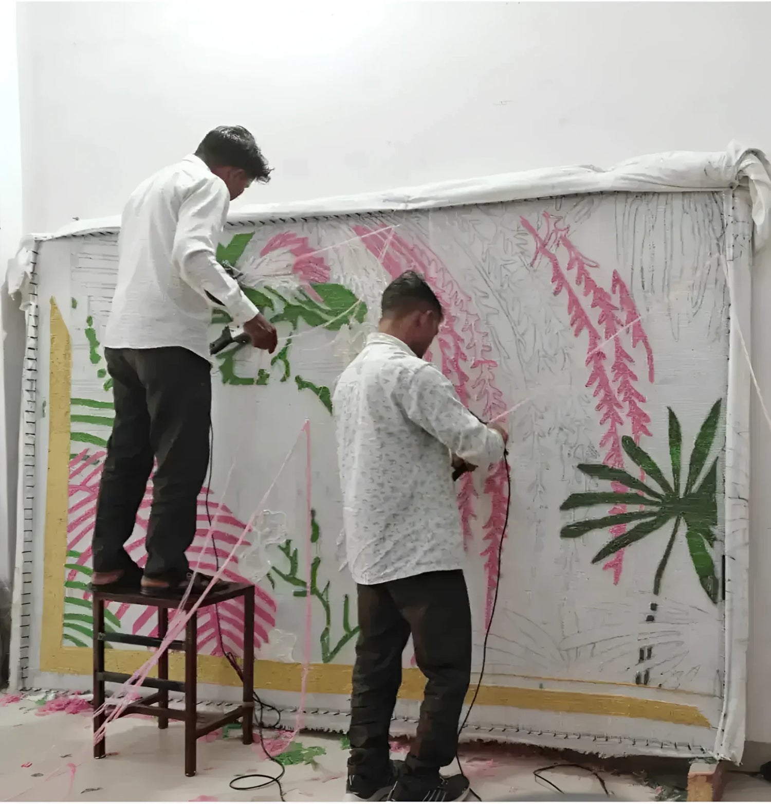 Artisans meticulously crafting a made-to-order hand-tufted wool rug, perfect for dining rooms and living room areas. The vibrant design, featuring green and pink patterns, illustrates the care and expertise involved in creating a luxurious area rug.