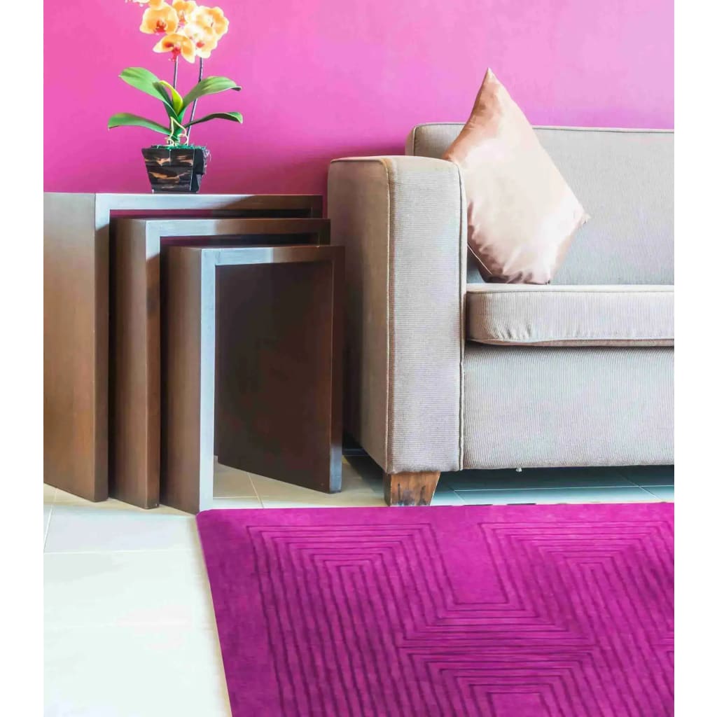 A vibrant magenta geometric wool area rug adds a pop of color to a contemporary dining room setting. The rug's modern design complements the sleek lines of the beige sofa and the wooden side tables, creating a stylish and inviting space. Perfect as a large area rug or a formal dining room carpet.