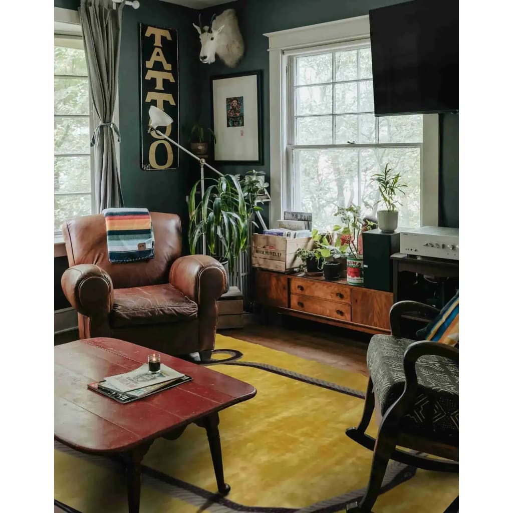 A stylish living room featuring a Magic Snake Gold Lush Hand Tufted Wool Rug. The area rug enhances the cozy space with its vintage design, perfect for large living rooms or offices. Surrounded by elegant furniture and indoor plants, this wool rug adds warmth and character.