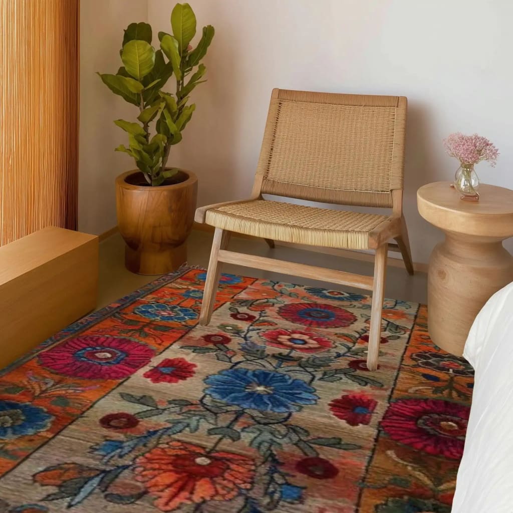 Bright and colorful Maharaja Garden Hand Tufted Area Rug displayed in a cozy bedroom setting. This wool rug features a vibrant floral pattern, perfect for adding a touch of elegance to your dining room or bedroom. The detailed design of the bedroom rug complements the natural tones of the wooden chair and side table, creating a harmonious and inviting atmosphere.