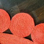 Close-up view of the Maia Classic Circles Round Jute Rug in red, showcasing its intricate woven design. This area rug is perfect for adding a touch of warmth and style to large living rooms. The round jute rug beautifully complements dark wooden floors, making it an ideal choice for those seeking unique living room area rugs.