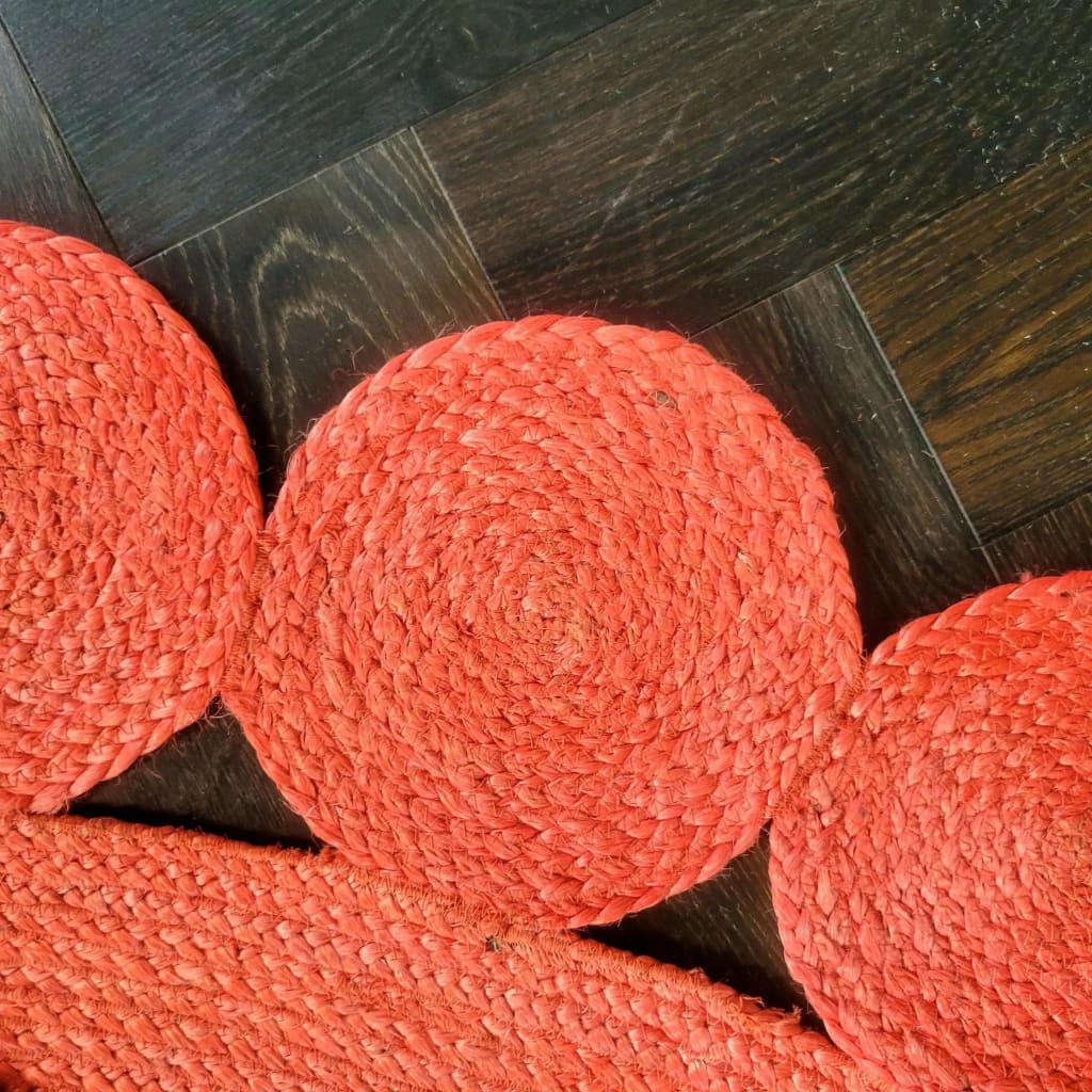 Close-up view of the Maia Classic Circles Round Jute Rug in red, showcasing its intricate woven design. This area rug is perfect for adding a touch of warmth and style to large living rooms. The round jute rug beautifully complements dark wooden floors, making it an ideal choice for those seeking unique living room area rugs.