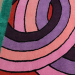 Close-up view of a contemporary wool area rug featuring vibrant, knotted circles in shades of pink, purple, and red on a green background. Perfect for adding a modern touch to living rooms or offices, this square rug offers a stylish and bold design.