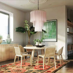 A stylish living room featuring the Majestic Blooms Hand Tufted Rug, which is an elegant area rug with a vintage floral design. The rug, perfect for large living rooms, measures 8x10 and is made of luxurious wool. It adds a touch of sophistication under a modern dining table set, surrounded by greenery and a chic chandelier.