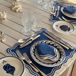 Marin Wave placemat close-up in navy blue with white wavy border, wave-patterned plate and shell-motif bread plate