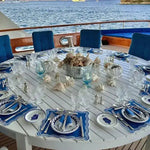 Marin Wave placemats in blue and white on a round table set on a yacht deck with ocean view and shell centerpiece