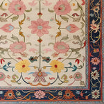A beautifully crafted Medallion Bloom Hand Knotted Area Rug featuring a vibrant floral design. The rug displays intricate pink, yellow, and blue flowers with green foliage on a cream background, bordered by a richly detailed navy edge. This vintage rug brings a touch of elegance to large living room spaces, resembling traditional Persian rugs.