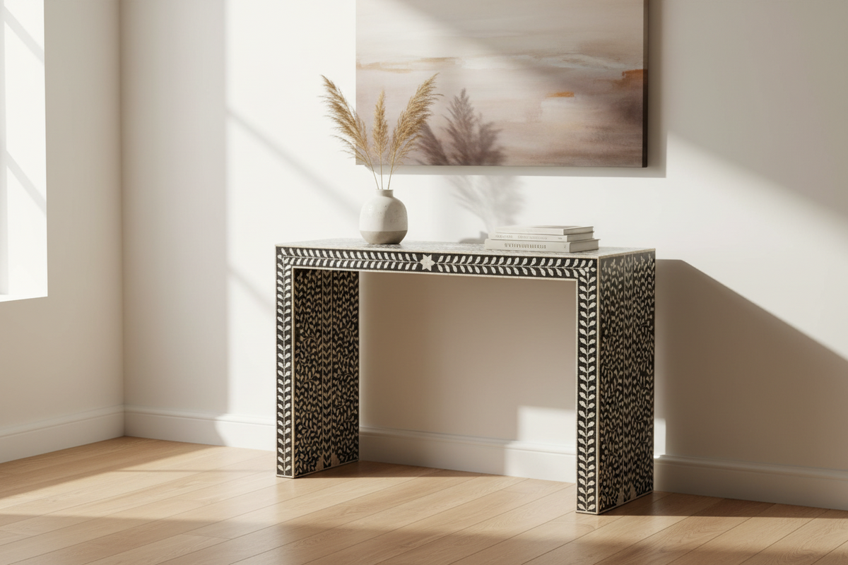 A bone-and-ivory console table with a geometric chevron pattern, styled in a bright room with a vase of pampas grass and a stack of books on top.