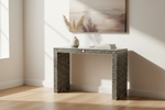 A bone-and-ivory console table with a geometric chevron pattern, styled in a bright room with a vase of pampas grass and a stack of books on top.
