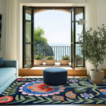 A vibrant Mexican Fiesta Hand Tufted Rug featuring a colorful floral design, enhancing the aesthetic of a bright living room. The area rug, ideal for living room rugs 8x10 or bedroom area rugs, adds a cozy touch to the space with its wool texture. The room showcases a serene view through open doors leading to a balcony, complementing the elegant blend of the rug's colors with the surrounding decor.