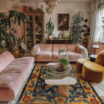 A cozy living room featuring the Midnight Blossom Heritage Hand Tufted Area Rug with a vibrant floral design. This vintage wool rug adds a touch of elegance to the space, complemented by plush pink sofas and lush green plants, perfect for dining room or living room settings.