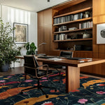 Stylish home office featuring a Midnight Garden hand tufted area rug with a vibrant floral pattern in a contemporary setting. The large living room rug adds a touch of vintage charm to the modern decor, complemented by wooden bookshelves and a sleek desk, creating a cozy, inviting atmosphere.