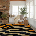 A contemporary wool area rug with an abstract tiger stripe pattern in black, orange, and beige, placed in a cozy living room. The room features a comfortable armchair, a rustic wooden side table, and a basket with greenery, complemented by a stone fireplace and large windows, creating a warm and inviting atmosphere. Ideal for adding a touch of style to large living room spaces.