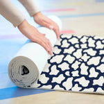Hands rolling up the navy and white patterned yoga mat, showing its cushioned thickness