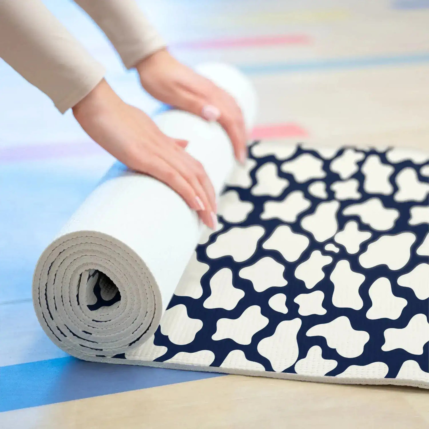 Hands rolling up the navy and white patterned yoga mat, showing its cushioned thickness
