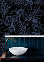Midnight Oasis dark navy wallpaper with blue tropical palm fronds in bathroom; marble vessel sink and brass faucet