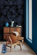 Midnight Oasis dark navy palm leaf wallpaper in corner setting; antique sideboard, blue glaze vase, sculpted wood chairs