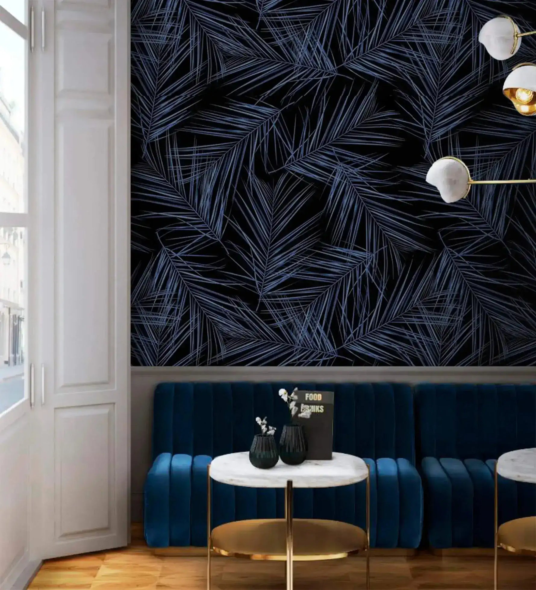 Midnight Oasis blue-black tropical leaf wallpaper in lounge; navy velvet banquette, gold marble side tables, globe pendants