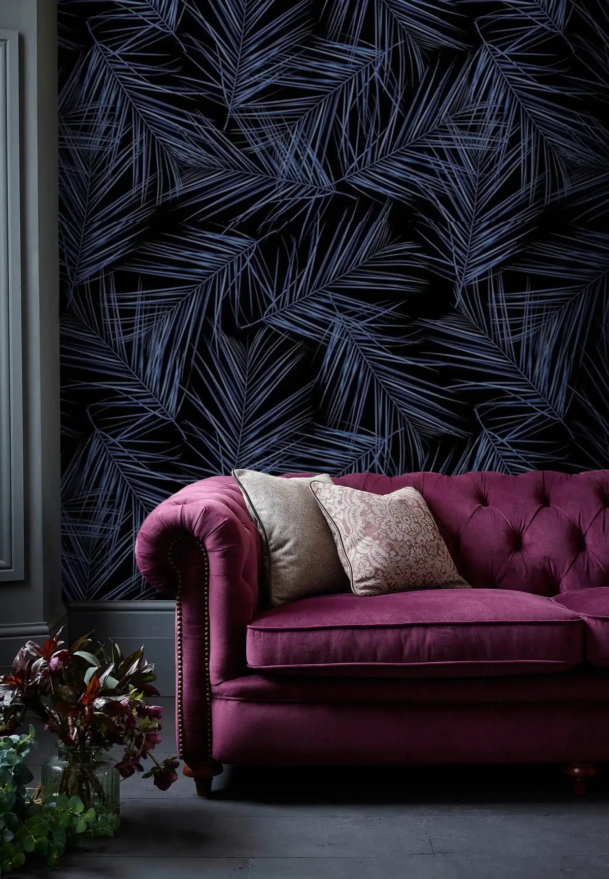 Midnight Oasis dark navy tropical palm wallpaper behind magenta velvet tufted Chesterfield sofa with neutral cushions