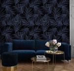 Midnight Oasis dark navy tropical leaf wallpaper behind navy velvet sofa; gold side tables, pink flowers, herringbone floor