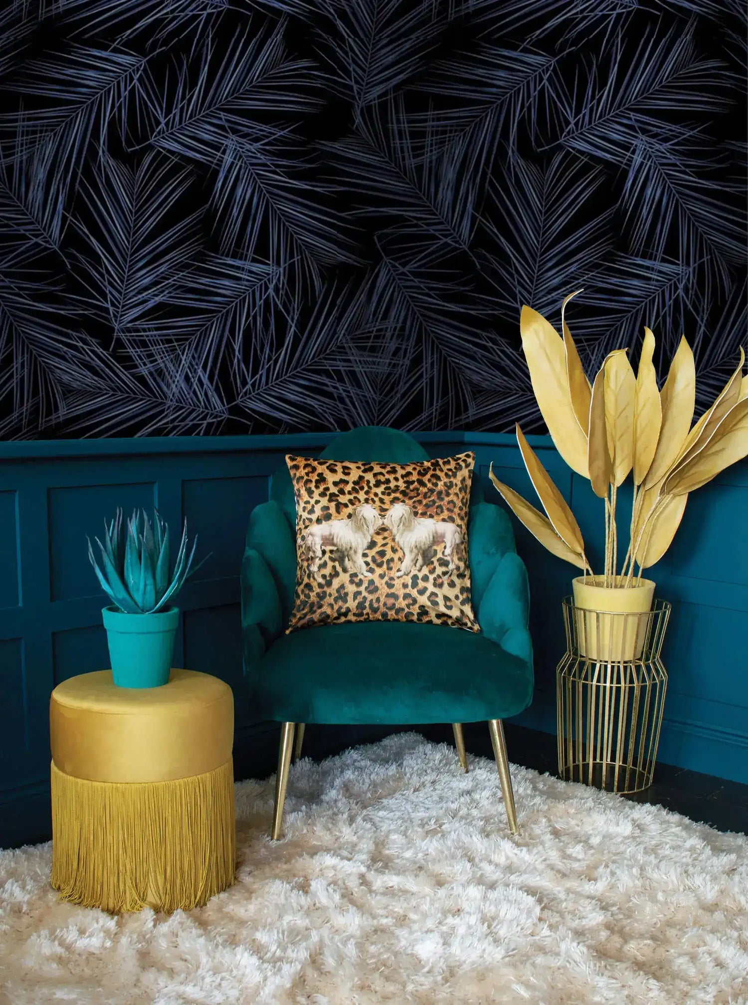 Midnight Oasis blue-black tropical leaves wallpaper above teal wainscoting; velvet armchair with leopard pillow and gold stool