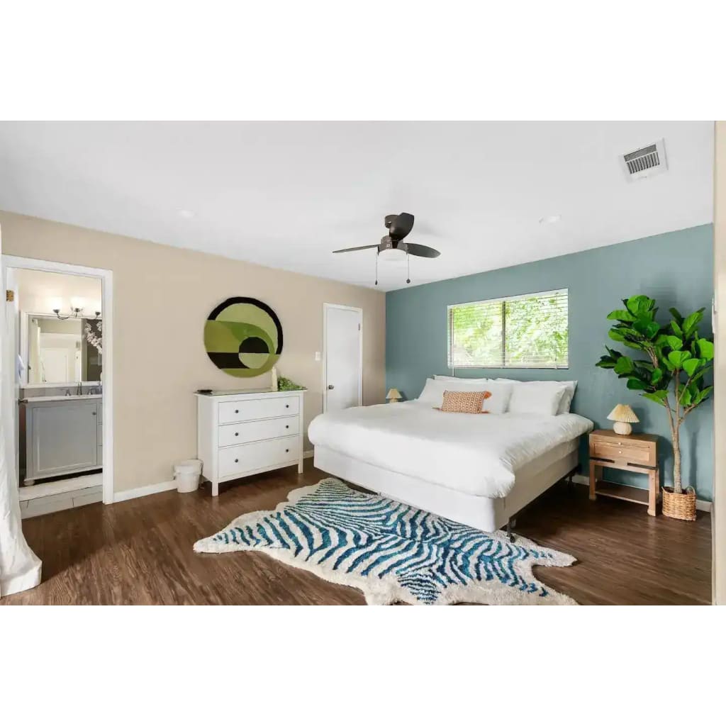 Stylish bedroom featuring a Mini Maia Geometric Round Hand Tufted Wool Rug with an abstract design. This area rug adds a modern touch to the room, perfect for large living rooms or offices. The wool rug complements the wooden flooring and white decor, enhancing the cozy and inviting atmosphere.