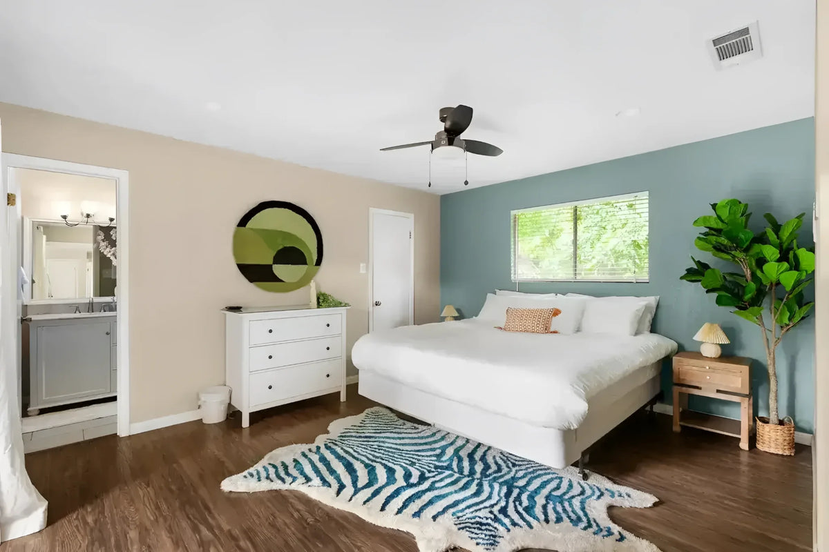 Stylish bedroom featuring a Mini Maia Geometric Round Hand Tufted Wool Rug with an abstract design. This area rug adds a modern touch to the room, perfect for large living rooms or offices. The wool rug complements the wooden flooring and white decor, enhancing the cozy and inviting atmosphere.