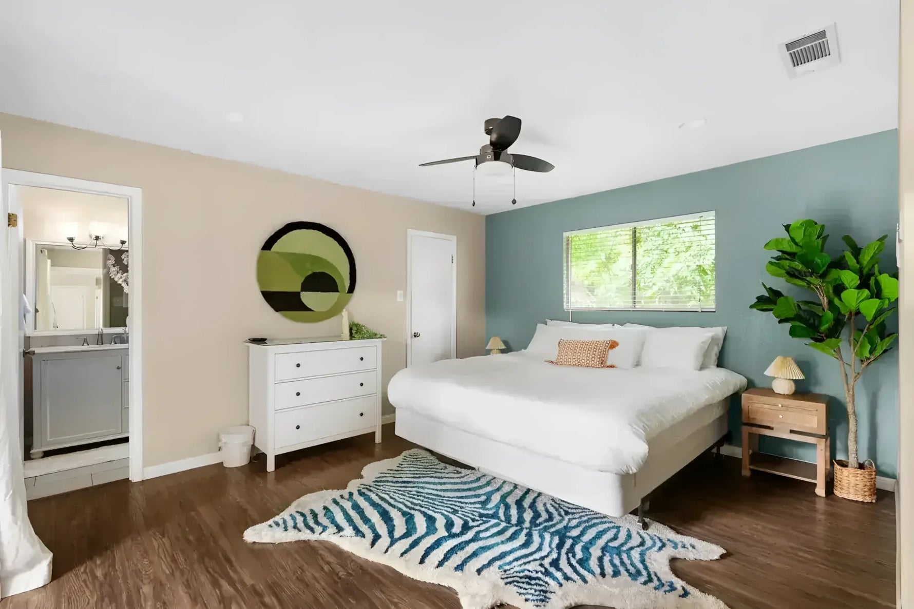 Stylish bedroom featuring a Mini Maia Geometric Round Hand Tufted Wool Rug with an abstract design. This area rug adds a modern touch to the room, perfect for large living rooms or offices. The wool rug complements the wooden flooring and white decor, enhancing the cozy and inviting atmosphere.