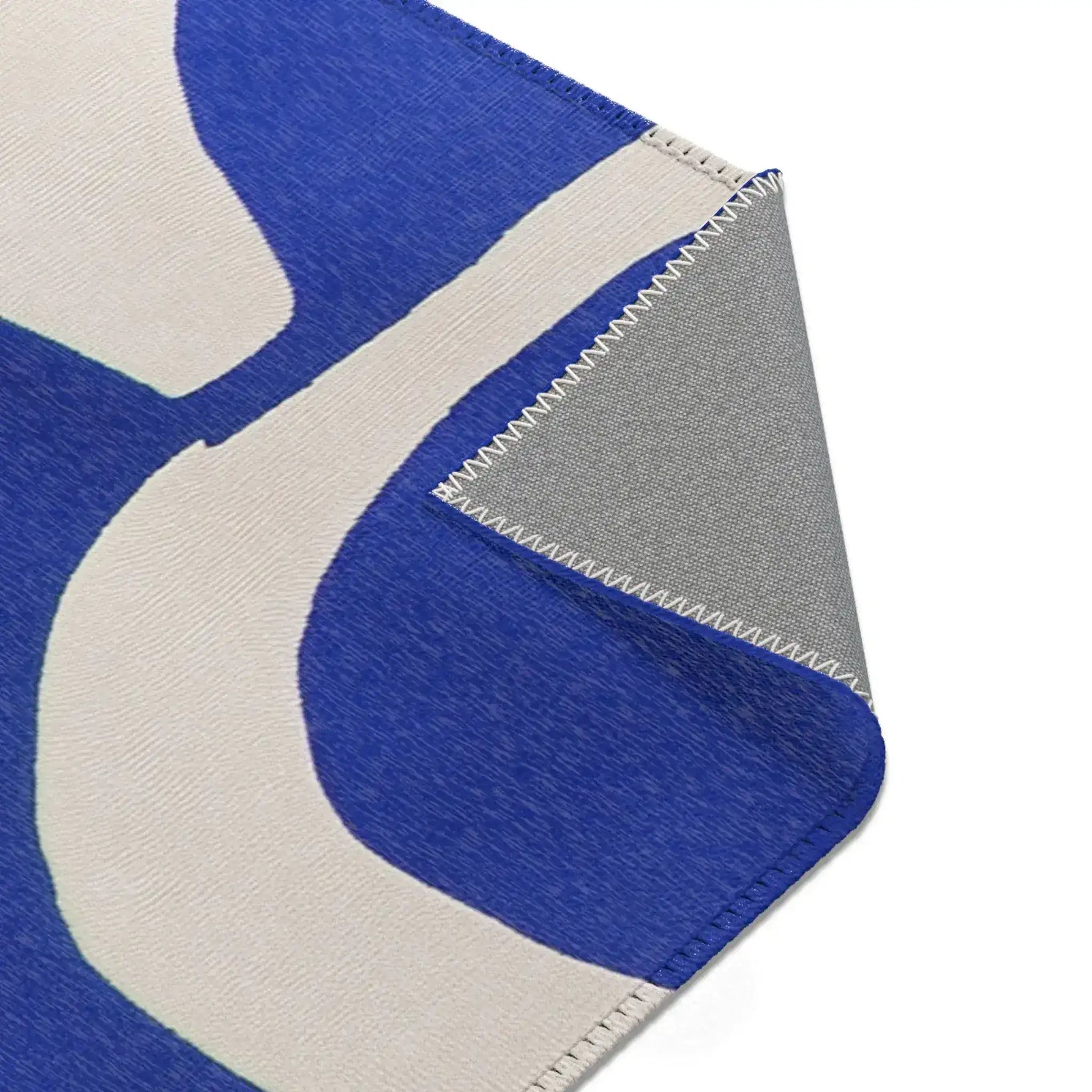 Modern Abstract Blue & White Rug bottom corner fold — arching cobalt shapes near edge with cream backing panel curling open