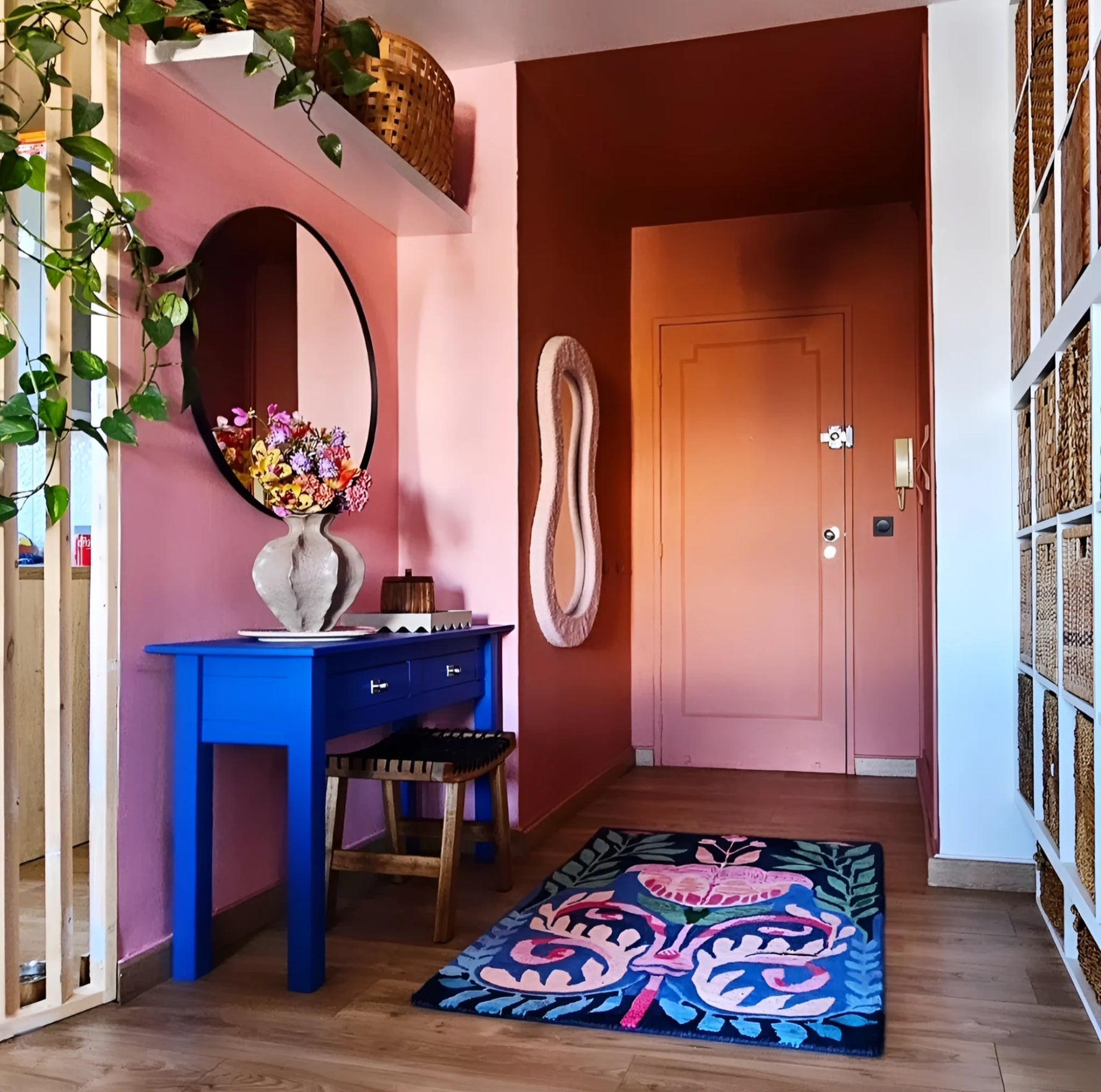 Modern interior with a blue console table, pink walls, and a colorful rug.