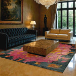 A luxurious living room featuring a modern tribal hard viscose hand knotted wool rug with vibrant abstract patterns. This contemporary area rug, perfect as a dining table rug in a dining room, adds a splash of color with its pink and dark hues. The elegant Persian-style design complements the plush furniture and opulent chandelier, creating a sophisticated ambiance.