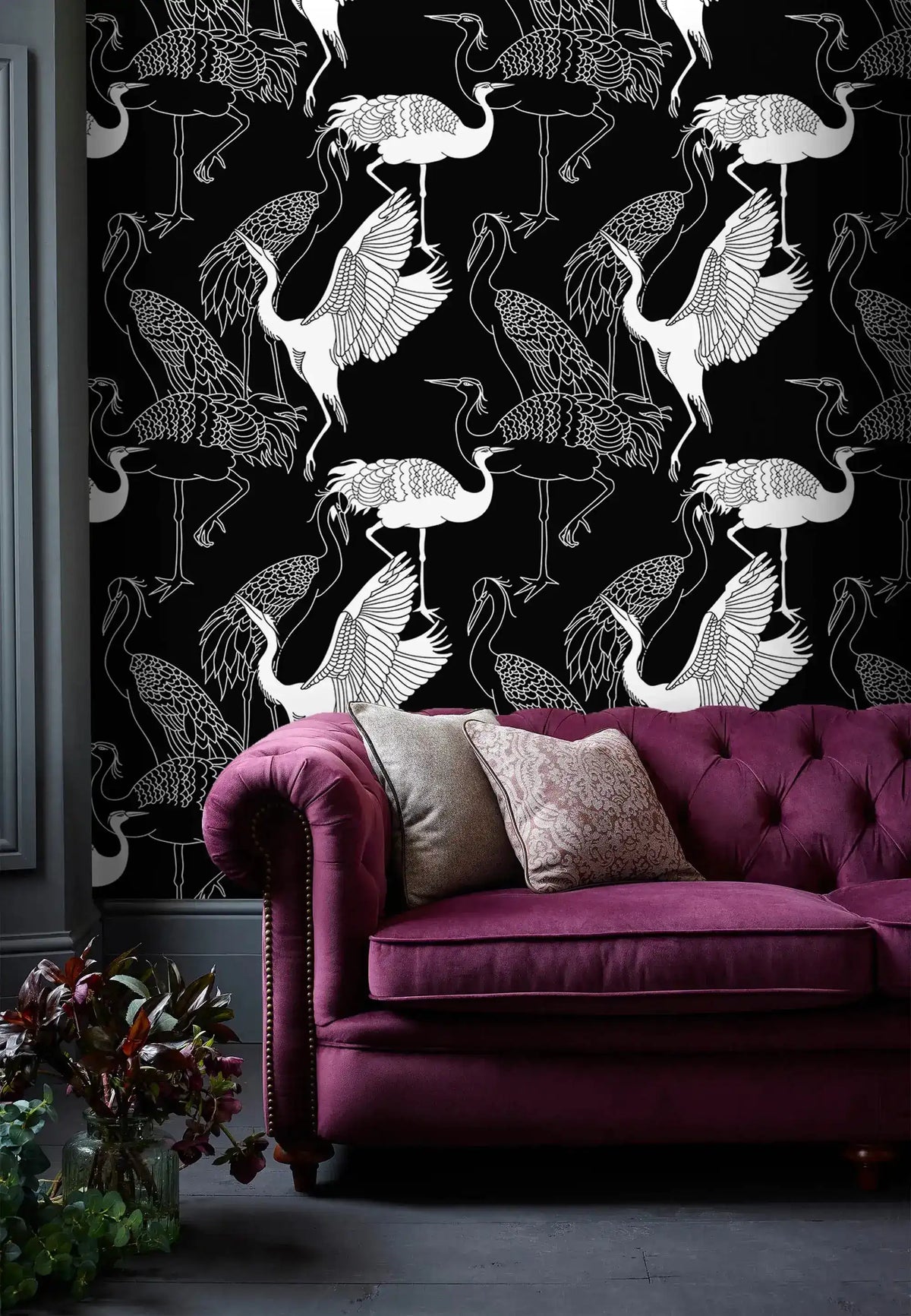 Monochrome crane wallpaper with white cranes on black behind a berry velvet tufted Chesterfield sofa