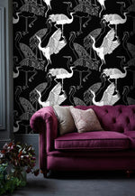 Monochrome crane wallpaper with white cranes on black behind a berry velvet tufted Chesterfield sofa