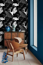 Monochrome crane wallpaper with white cranes on black beside a blue wall and carved wood cabinet