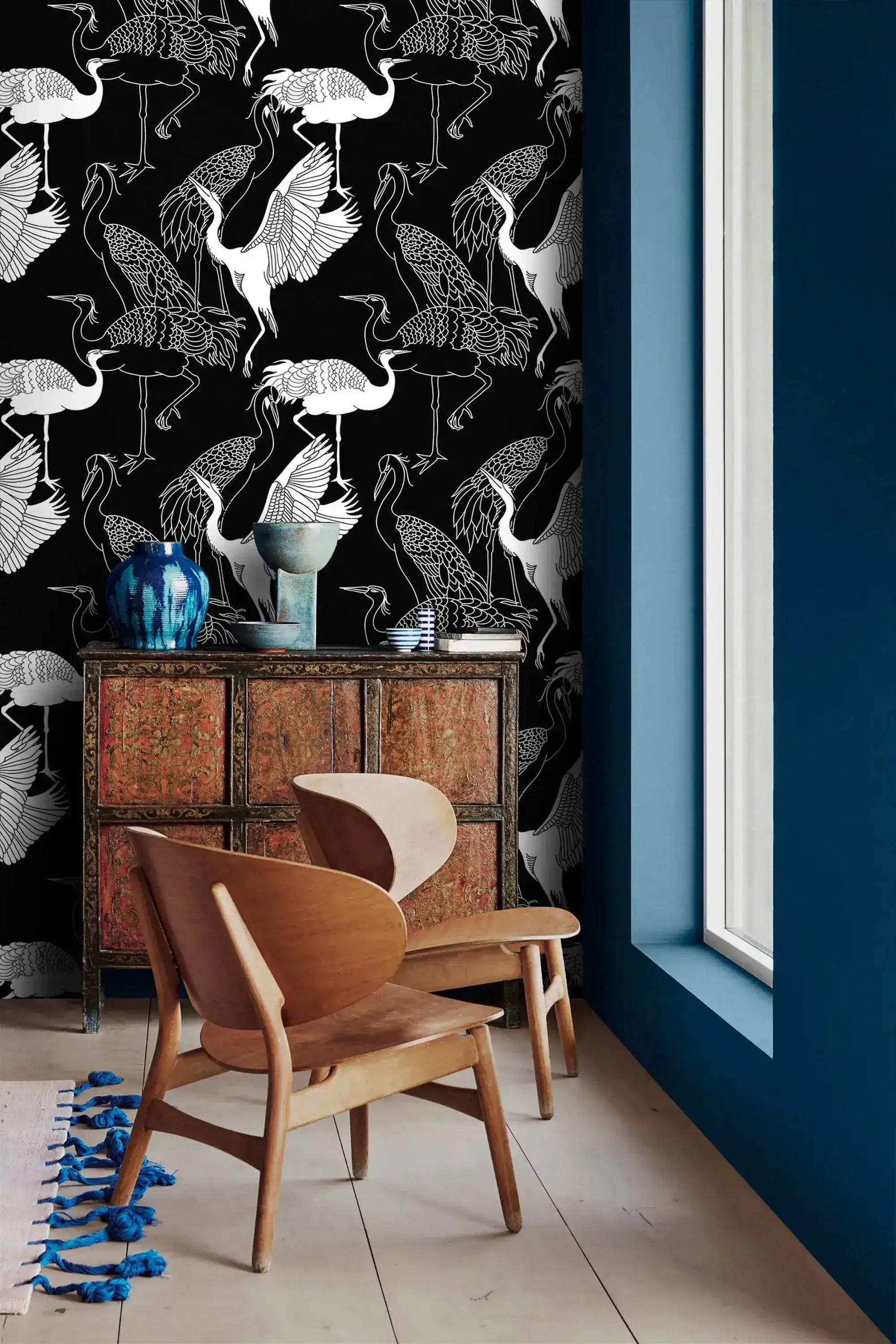 Monochrome crane wallpaper with white cranes on black beside a blue wall and carved wood cabinet